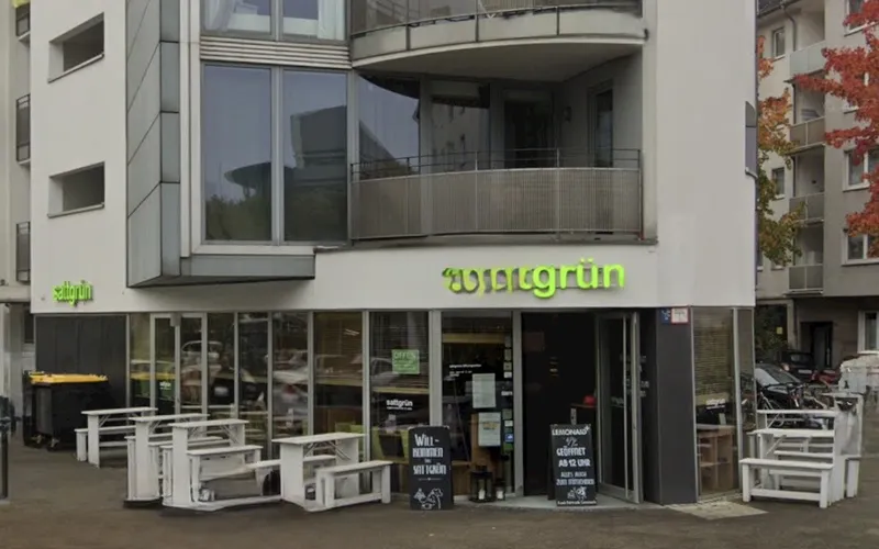 Erdgeschoss des Restaurants sattgrün in Düsseldorf-Flingern mit grün leuchtendem Schriftzug über dem Eingang und weißen Außentischen davor.