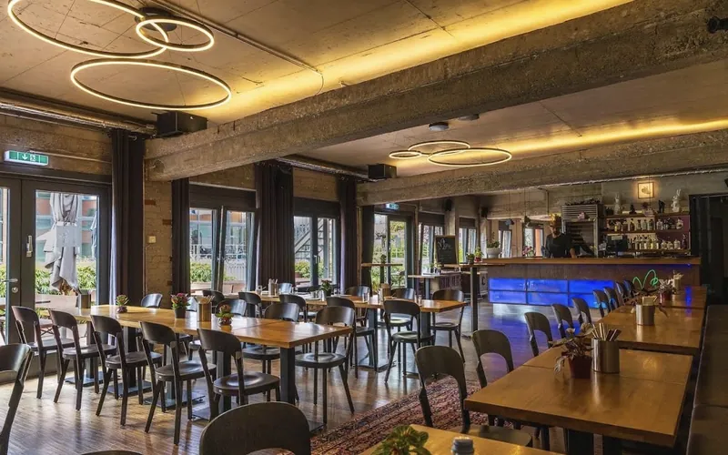 Industriel gestalteter Gastraum von Hase & Igel in den Schwanenhöfen mit leuchtend grünem Hasen-Symbol über der Bar.
