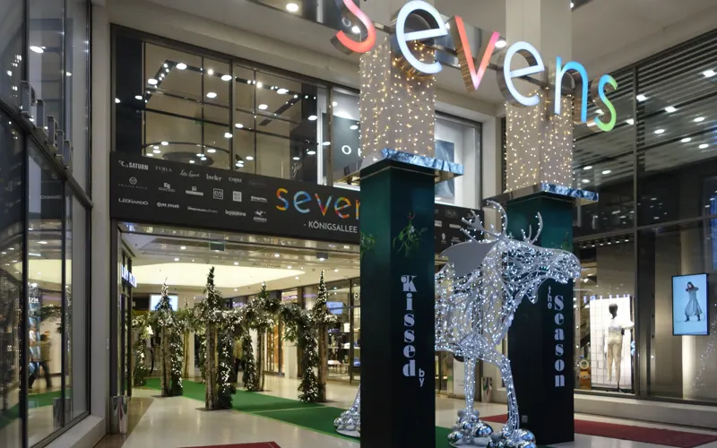 Eingang des Einkaufscenters sevens auf der Königsallee mit beleuchtetem Schriftzug.